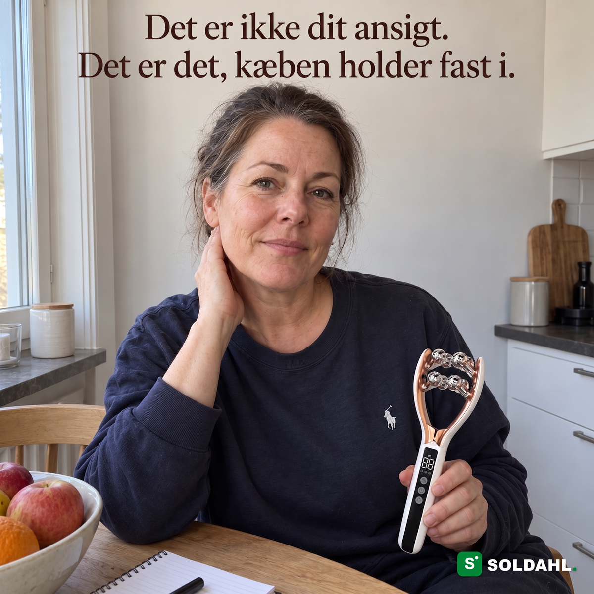 Kvinde ved køkkenbordet med hånden mod kæben holder Kæbero i skødet