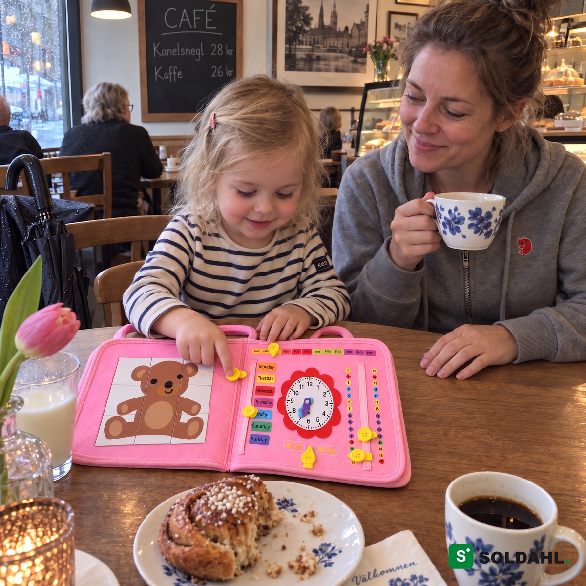 Treårig på café knapper i aktivitetsbogen, mens mor drikker kaffe
