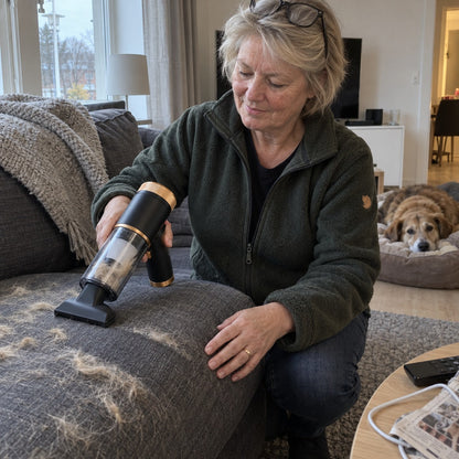 Kvinde tager hundehår fra sofaen med Sugro, mens hunden hviler i baggrunden